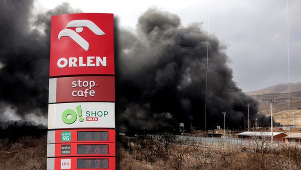 Pylon Orlenu z cenami paliw na tle pożaru rafinerii koło Teheranu