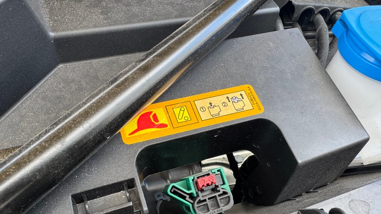 Naklejka pod maską samochodu, która pokazuje instrukcję odłączenia prądu w samochodzie