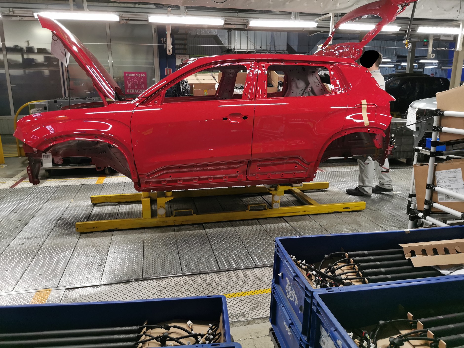 Nadwozie "dowiezione" przez system dźwigów i wyciągów na teren montowni – tuż po lakierowaniu – ma jeszcze drzwi i inne elementy ruchome. Na tym etapie drzwi są zdejmowane z karoserii, aby ułatwić dostęp do wnętrza, zmniejszyć ilość potrzebnej przestrzeni i zredukować ryzyko powstania uszkodzeń lakierniczych. Co ciekawe, po uzbrojeniu karoserii wrócą do niej te same drzwi i klapy, które uprzednio były zdjęte. Ten proces jest synchronizowany, w każdym innym wypadku nie sposób byłoby uniknąć problemów z dopasowaniem oraz minimalnych różnic w odcieniach.