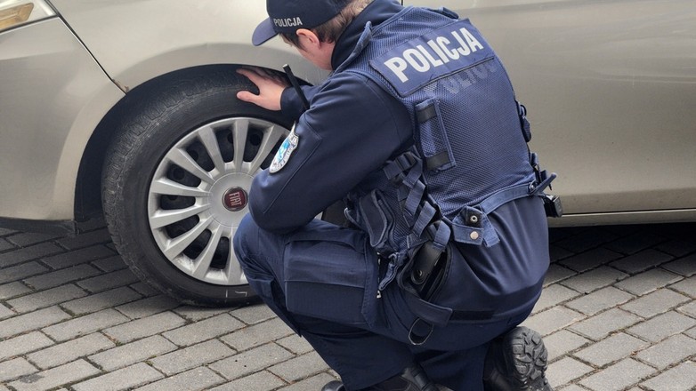 Policjant kontroluje stan ogumienia w samochodzie