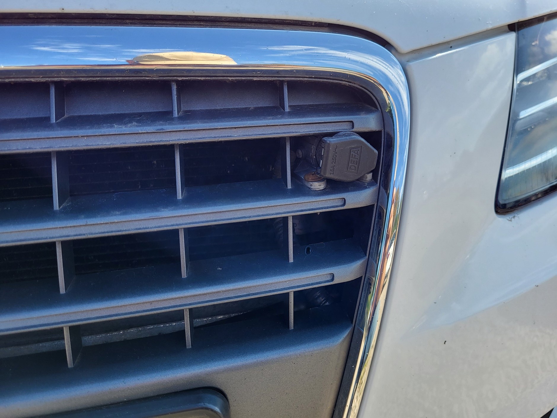 Audi A4 Avant Quattro - biały "szwed" z silnikiem benzynowym. Miły sprzedawca, ale auto pokolizyjne i podrdzewiałe. Na zdjęciu gniazdo elektrycznego podgrzewacza silnika/wnętrza – typowa rzecz w Skandynawii