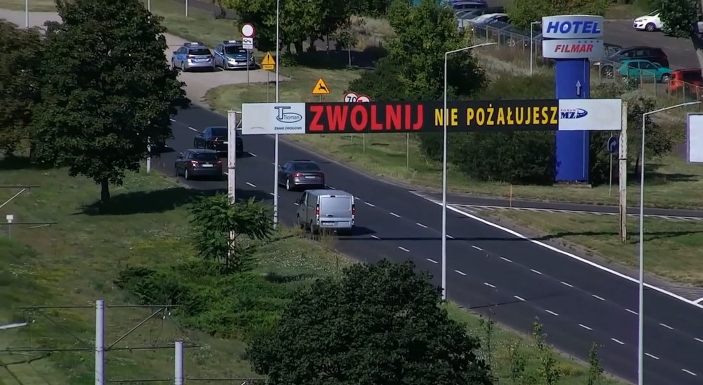 Znak nawołujący do zwolnienia a za nim patrol policji