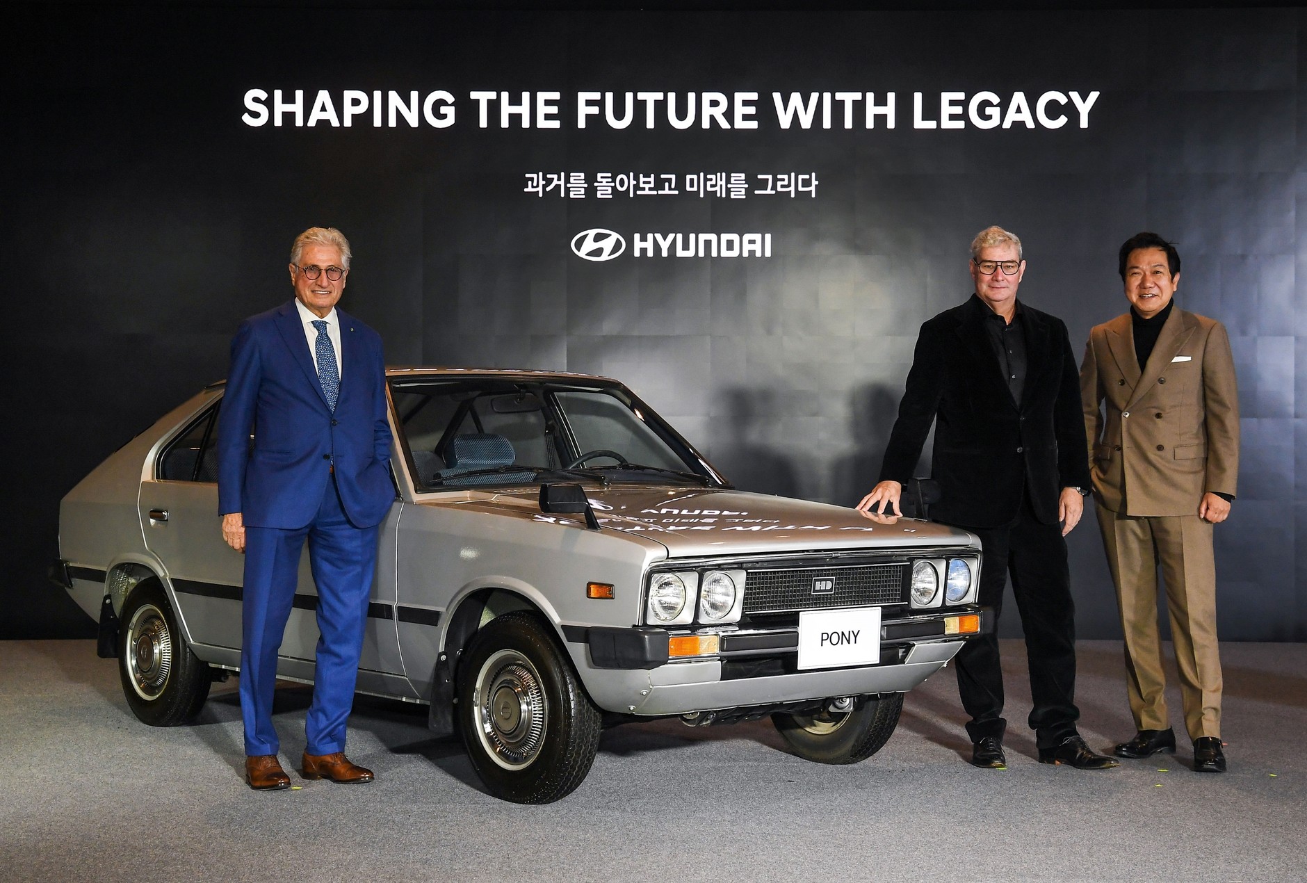 Od lewej Giorgio Giugiaro oraz Luc Donckerwolke i SangYup Lee, dwaj najważniejsi styliści Hyundaia. Między nimi Hyundai Pony I (1975-1981).