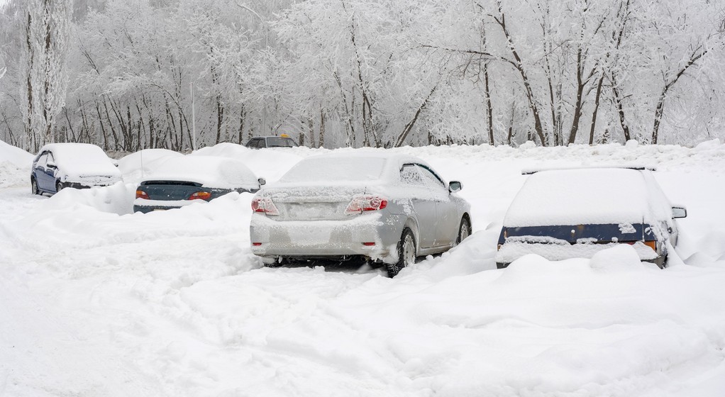 Zasypane śniegiem samochody na nieodśnieżonym parkingu