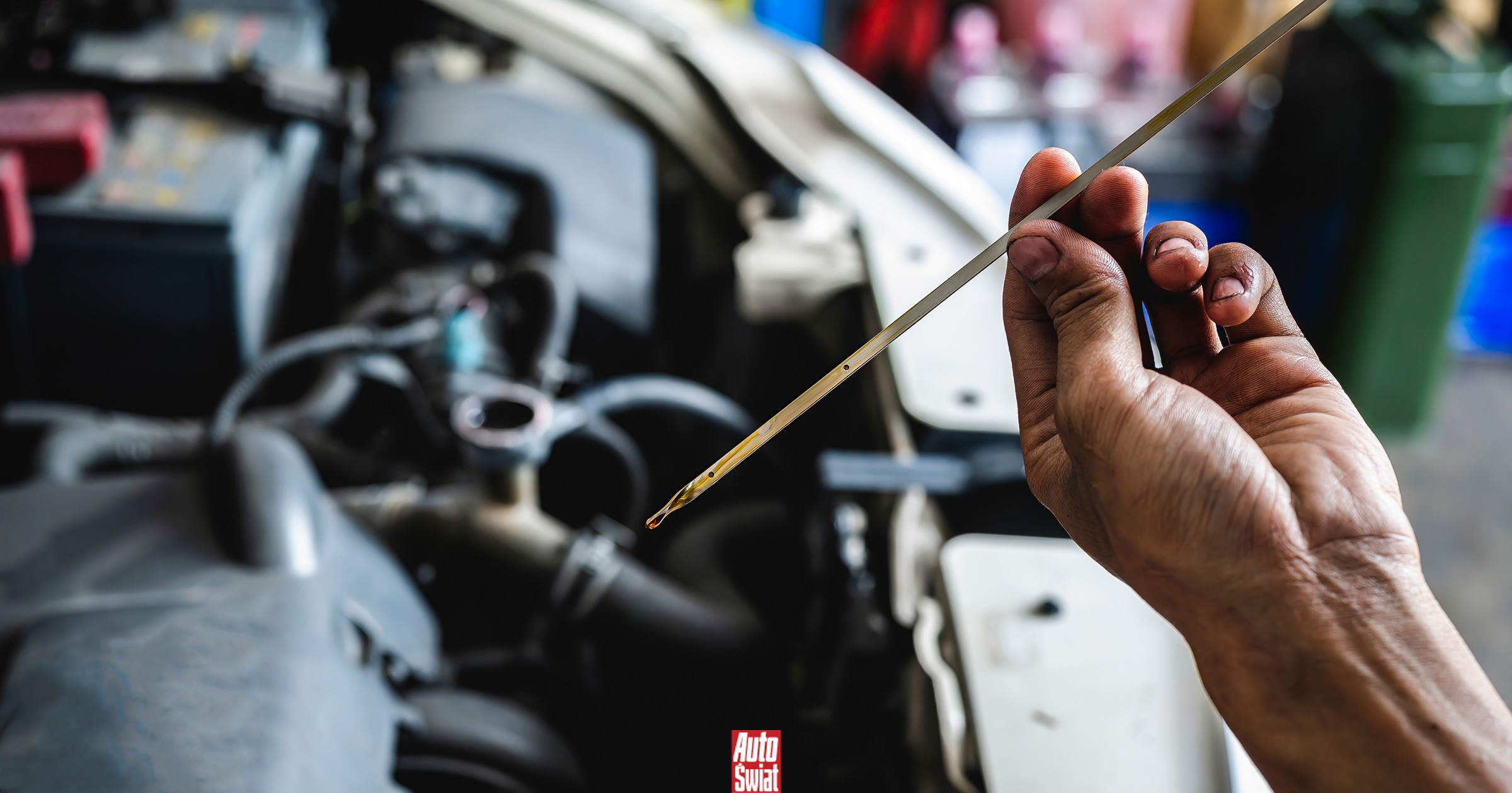 Un motore con olio che esce, con un'auto e un tecnico che controlla il livello