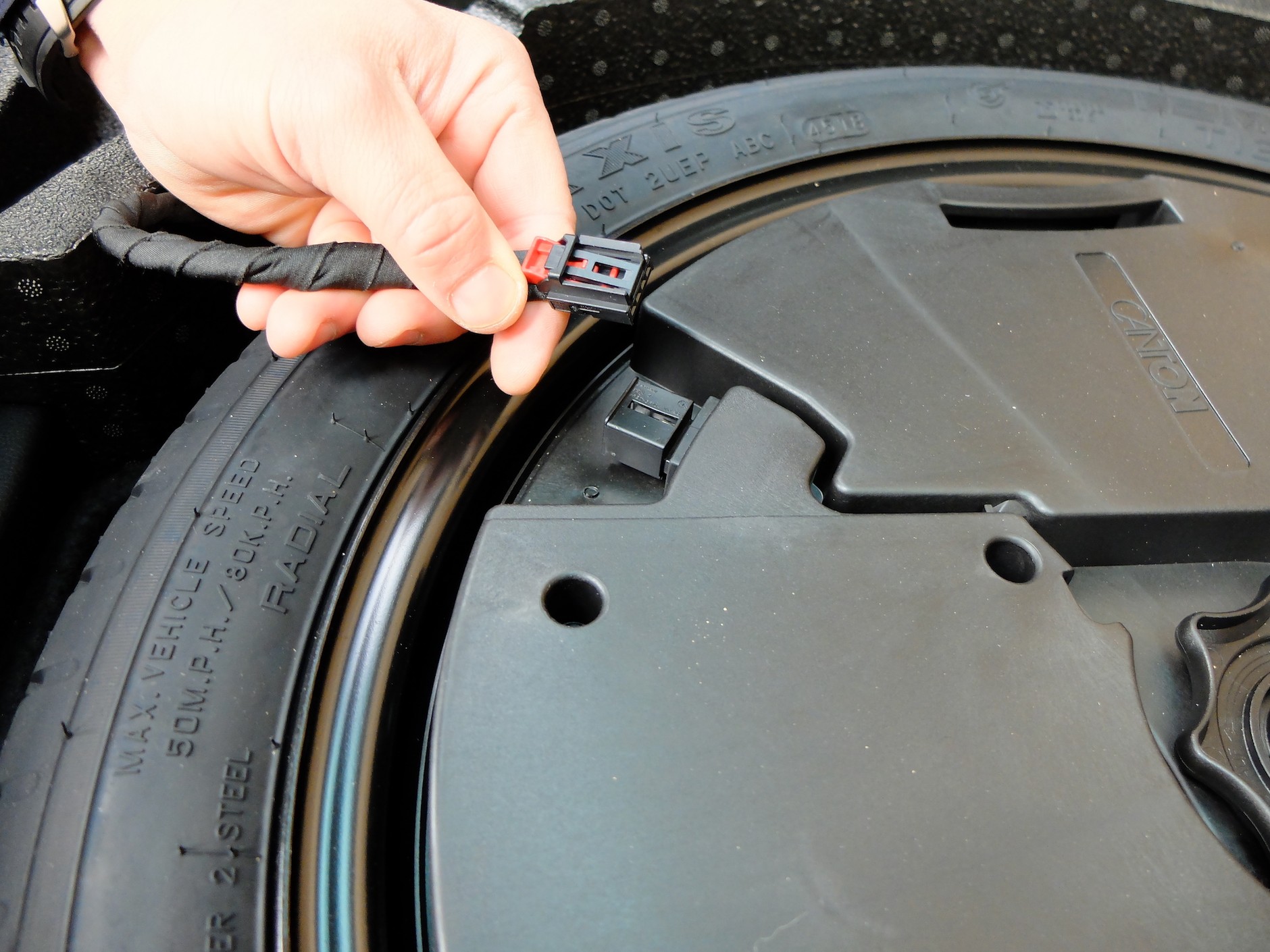 Wymiana koła krok po kroku: ostrożnie, nie na siłę, wypnij kostkę elektryczną doprowadzającą zasilanie do subwoofera umieszczonego wewnątrz koła zapasowego.