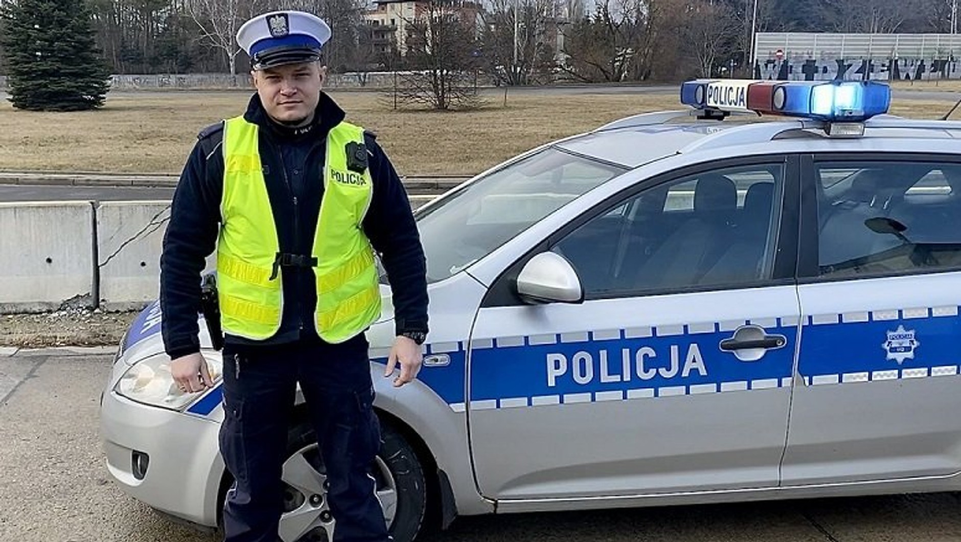 Policjant z łódzkiej drogówki na tle radiowozu na sygnale