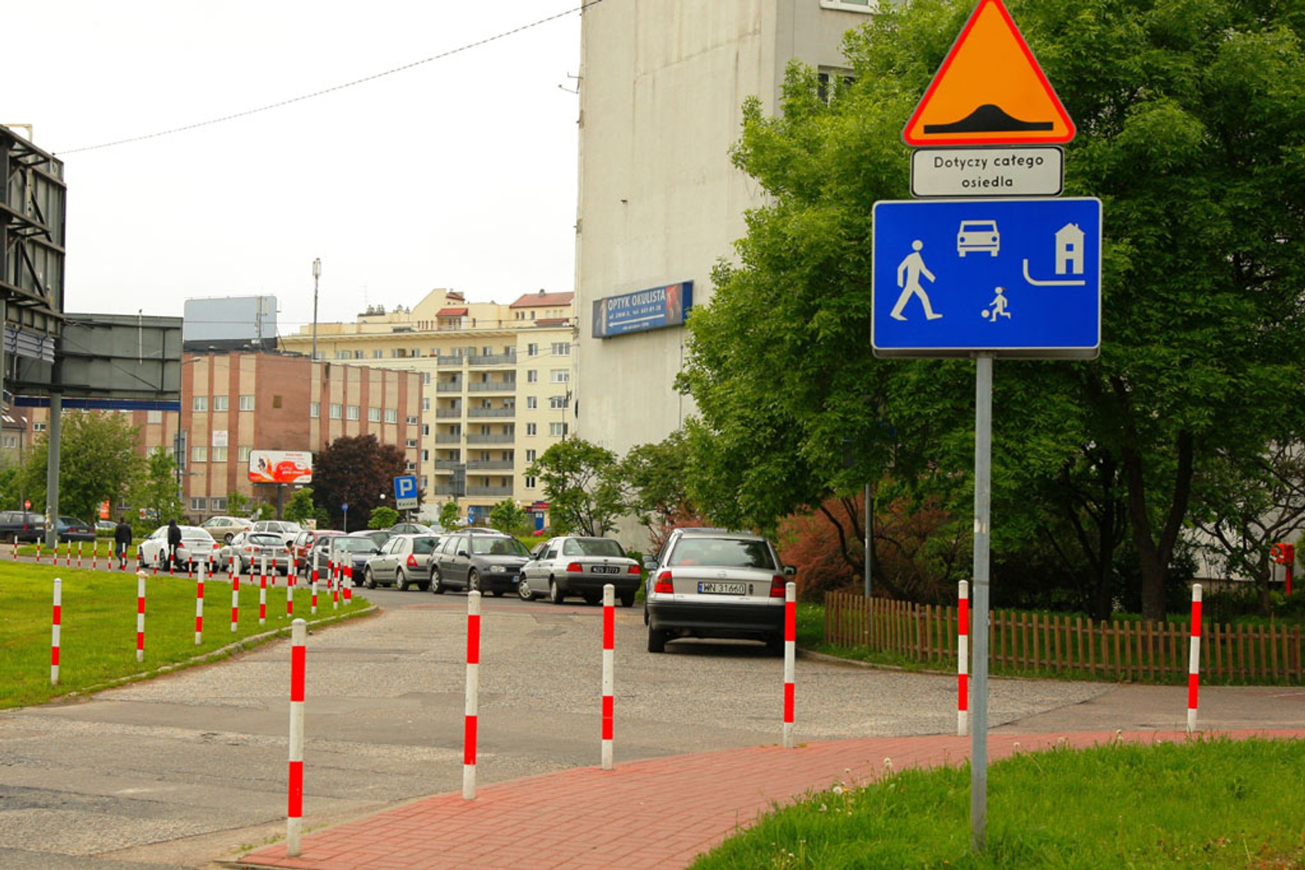 Strefa zamieszkania (znak D-40): piesi mają pierwszeństwo, a parkować wolno tylko w wyznaczonych miejscach, czyli zupełnie inaczej niż na tym zdjęciu. Informacja o progach zwalniających jest tu zbędna, bo w strefie zamieszkania można je ustawiać bez ostrzeżenia. 