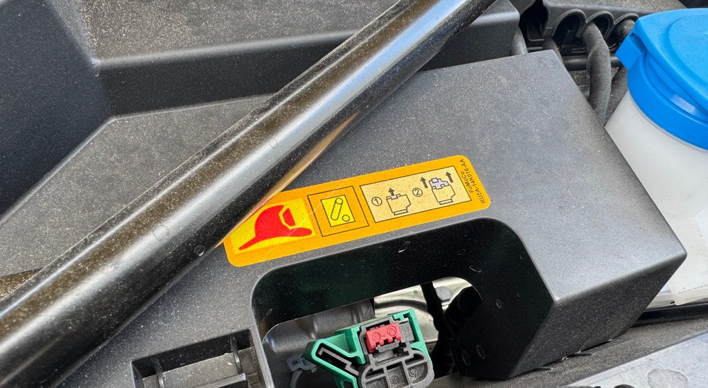 Naklejka pod maską samochodu, która pokazuje instrukcję odłączenia prądu w samochodzie