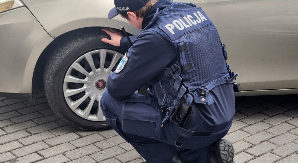 Policjant kontroluje stan ogumienia w samochodzie