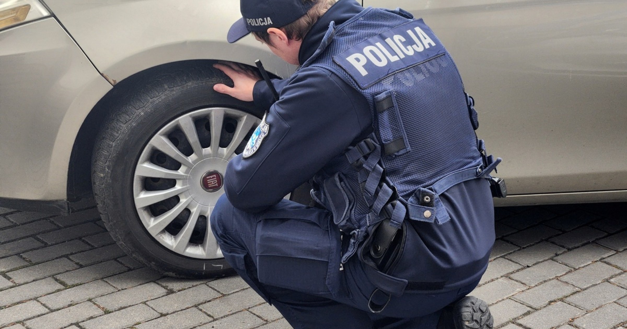 Policjant kontrolujący stan opon w samochodzie. Jazda na zimowych oponach latem może być niebezpieczna