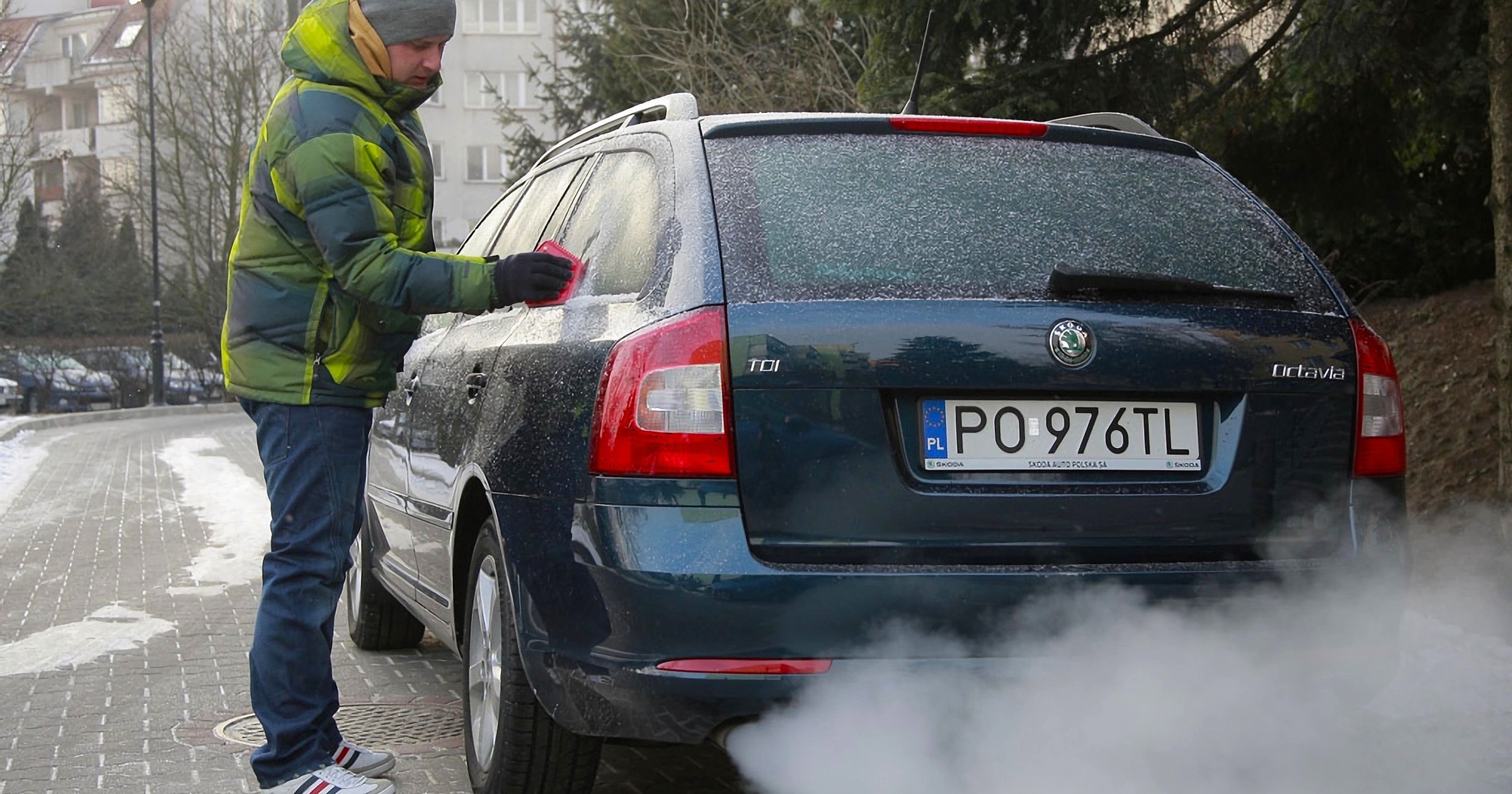 Kierowca w kurtce zimowej zeskrobuje lód z szyb samochodu
