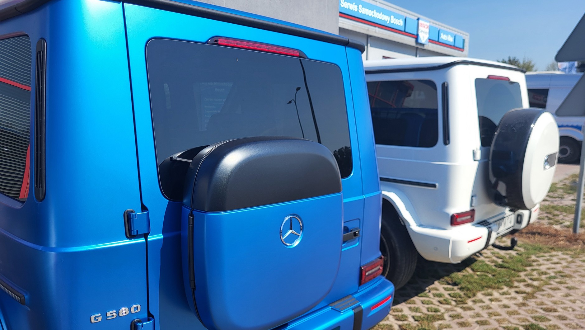 Nie, elektryczny Mercedes G580 EQ nie ma na tylnej klapie kwadratowej dojazdówki – to schowek na kable! Na drugim planie wersja spalinowa z kołem zapasowym.