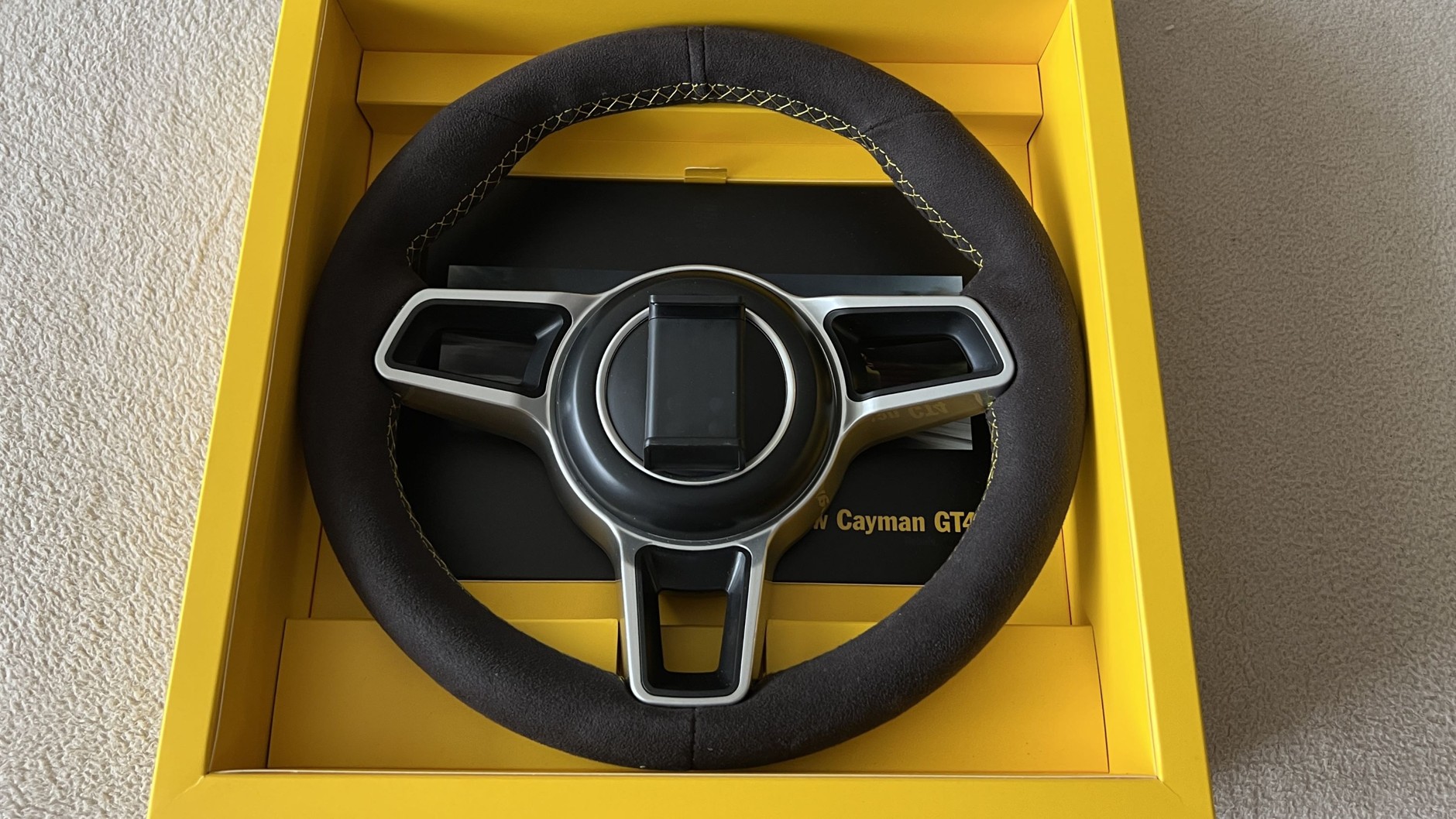 Prospekt Porsche Caymana GT4 z kierownicą, do której montuje się kompatybilnego smartfona, aby grać w symulacje wyścigów