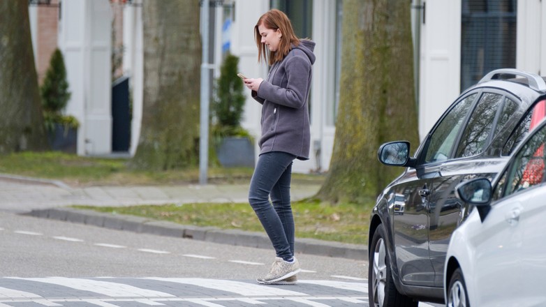 Pieszy ze smartfonem na przejściu przez jezdnię - zdjęcie ilustracyjne