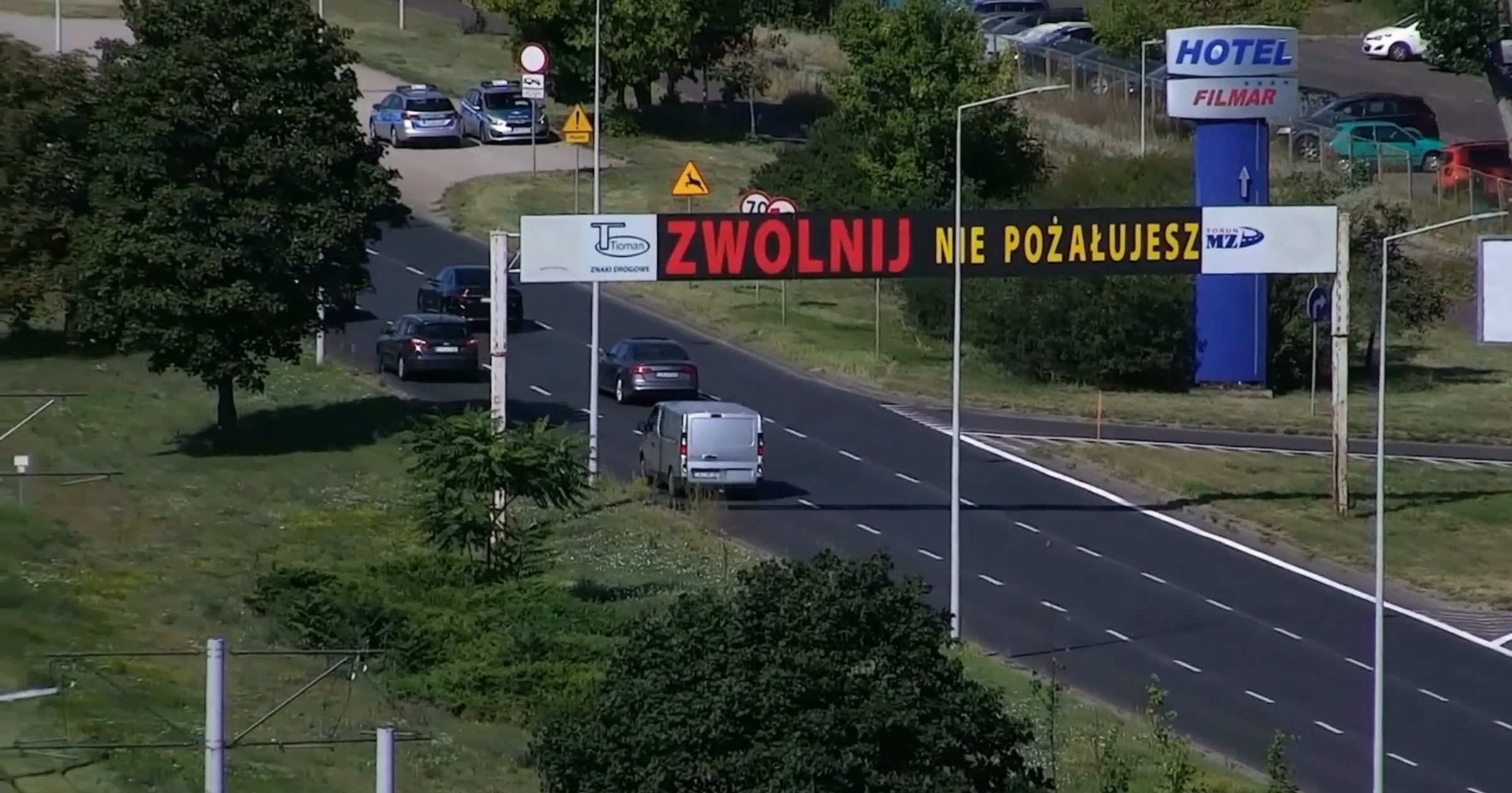 Znak nawołujący do zwolnienia a za nim patrol policji