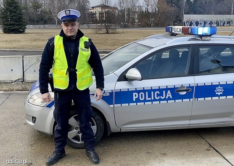 Policjant z łódzkiej drogówki na tle radiowozu na sygnale