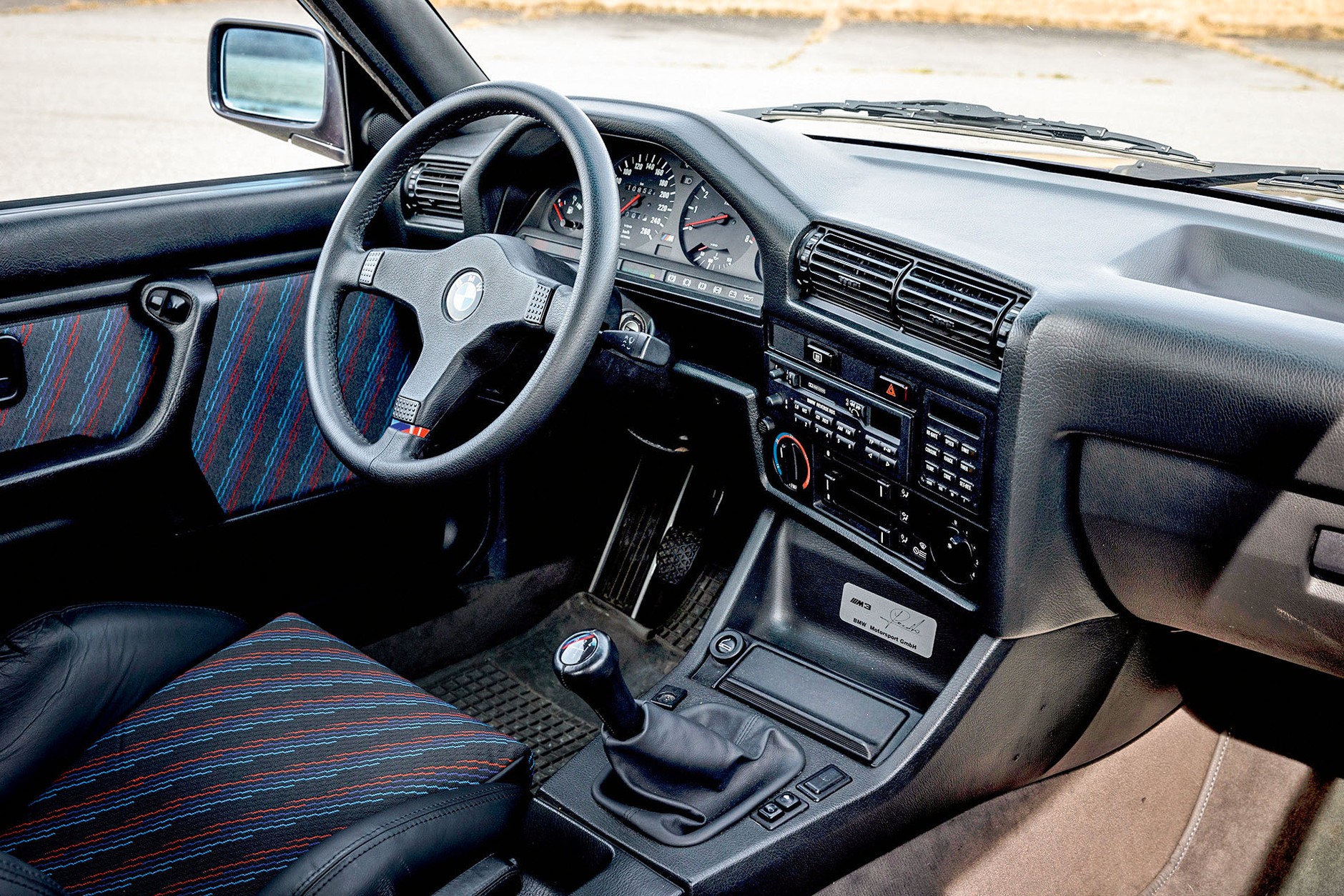 Sportowe siedzenia w kolorach M, pierwszy bieg w lewo i do tyłu. Typowa architektura E30: delikatność i skromność przeciwstawiona dzisiejszemu przesytowi.